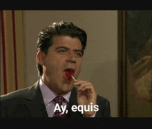 a man in a suit and tie is licking a lollipop and saying ay equis .