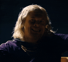 a man with blonde hair is wearing a purple shirt