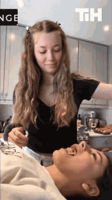 a woman in a black shirt is standing next to another woman in a kitchen with a sign that says th on it