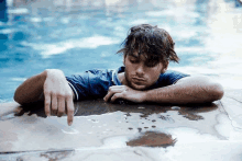 a man in a blue shirt is laying on the edge of a swimming pool