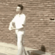 a man in a white shirt is standing in front of a brick wall and holding something .