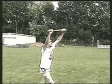 a man throwing a frisbee in a field with trees in the background and a white building in the background