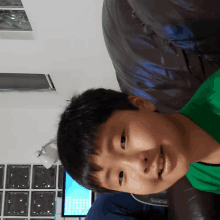 a young boy in a green shirt is smiling in front of a computer monitor