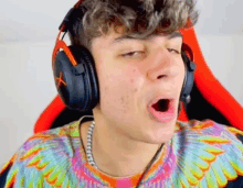 a young man wearing headphones and a colorful shirt is yawning .