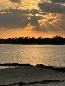 a sunset over a body of water with the sun shining through the clouds