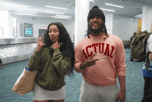 a man wearing a pink shirt that says actual stands next to a woman