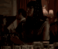 a woman in a white dress is sitting at a table in a dark room holding a glass of wine .