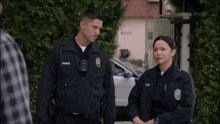 a man and a woman in police uniforms are standing next to each other in front of a building .