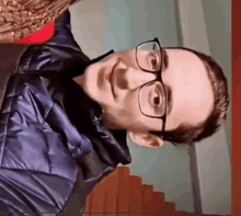 a young man wearing glasses and a blue jacket is standing in front of some stairs .