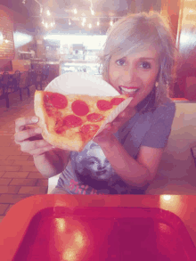 a woman is eating a slice of pepperoni pizza in a restaurant