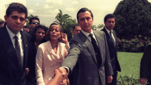 a man in a suit and tie shakes hands with a woman in a pink jacket