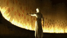 a man in a white robe is standing in front of a wall of flames .