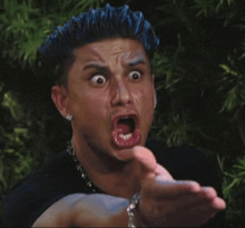 a man with blue hair is making a funny face with his mouth open .