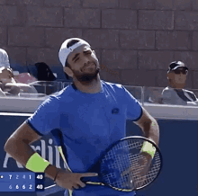 a man wearing a blue shirt and white hat is covering his face with his hand while holding a tennis racquet ..