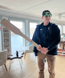 a man wearing a hat and glasses holds a large wooden stick