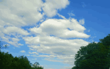 a blue sky with white clouds in it and trees in the foreground