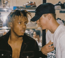 a man wearing an adidas shirt talks to another man in a hat