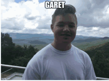 a young man in a white shirt stands in front of a mountain range with the name garet written on the bottom