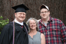 a man in a graduation cap and gown poses for a photo with his parents