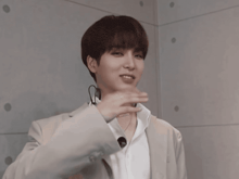 a man wearing a white shirt and a grey jacket is making a hand gesture