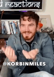 a man in a denim jacket is sitting in front of a bookshelf with a sign that says reactions .