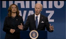 a man in a suit and tie stands at a podium with a woman behind him in front of a sign that says vaz