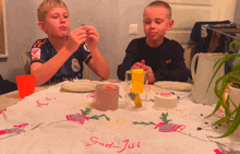 two boys sit at a table with a table cloth that says " god jul "