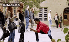 a man in a red shirt is kneeling down in front of a group of people walking down a street .