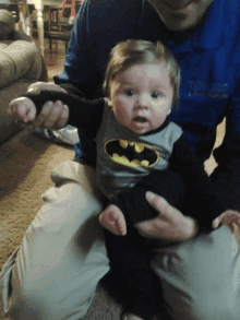 a man is holding a baby wearing a batman shirt