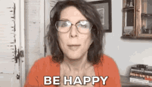 a woman wearing glasses is saying `` be happy '' while standing in front of a mirror .