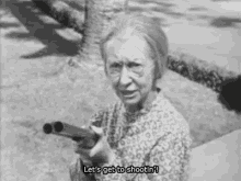 a black and white photo of an elderly woman holding a shotgun and saying `` let 's get to shootin '' .