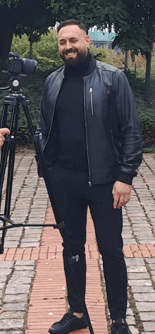 a man in a leather jacket stands in front of a camera