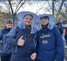 a boy wearing a napapijri jacket stands next to another boy wearing a bee hat