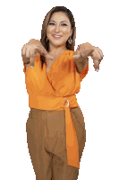 a woman in an orange top and brown pants points her fingers at the camera