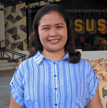 a woman in a blue shirt smiles in front of a stage that says sus