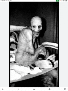 a black and white photo of a person with a scary face sitting on a bed .