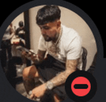 a man with tattoos is sitting in a chair looking at his phone