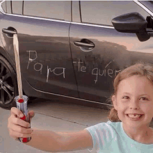 a little girl is holding a screwdriver in front of a car that has the word para written on the door