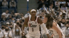 two women are playing basketball in front of a crowd and one of them is wearing a uconn jersey .