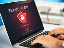 a person is typing on a laptop with a fraud alert displayed on the screen