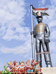 a statue of a man holding a flag is surrounded by a group of dwarfs