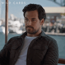 a man with a beard is wearing a jacket and a white shirt with the words wild cards below him