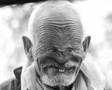 a black and white photo of an elderly man with a beard and missing teeth making a funny face .