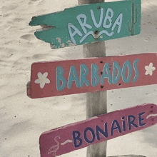 three wooden signs on a wooden post on the beach indicate aruba barbados and bonaire