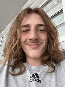 a young man with long hair and a mustache wears an adidas shirt