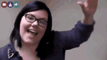 a woman wearing glasses is smiling and waving her arm in the air