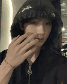 a young man wearing a black hoodie and a bracelet is holding his hand to his face .