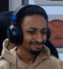 a man wearing headphones and a hoodie is smiling while sitting in a chair .