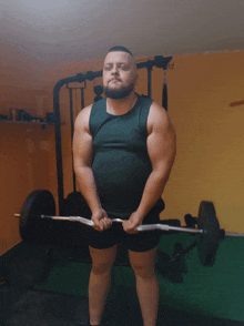 a man in a green tank top is holding a barbell in a gym