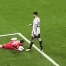 a soccer player is laying on the ground while another player kicks the ball .